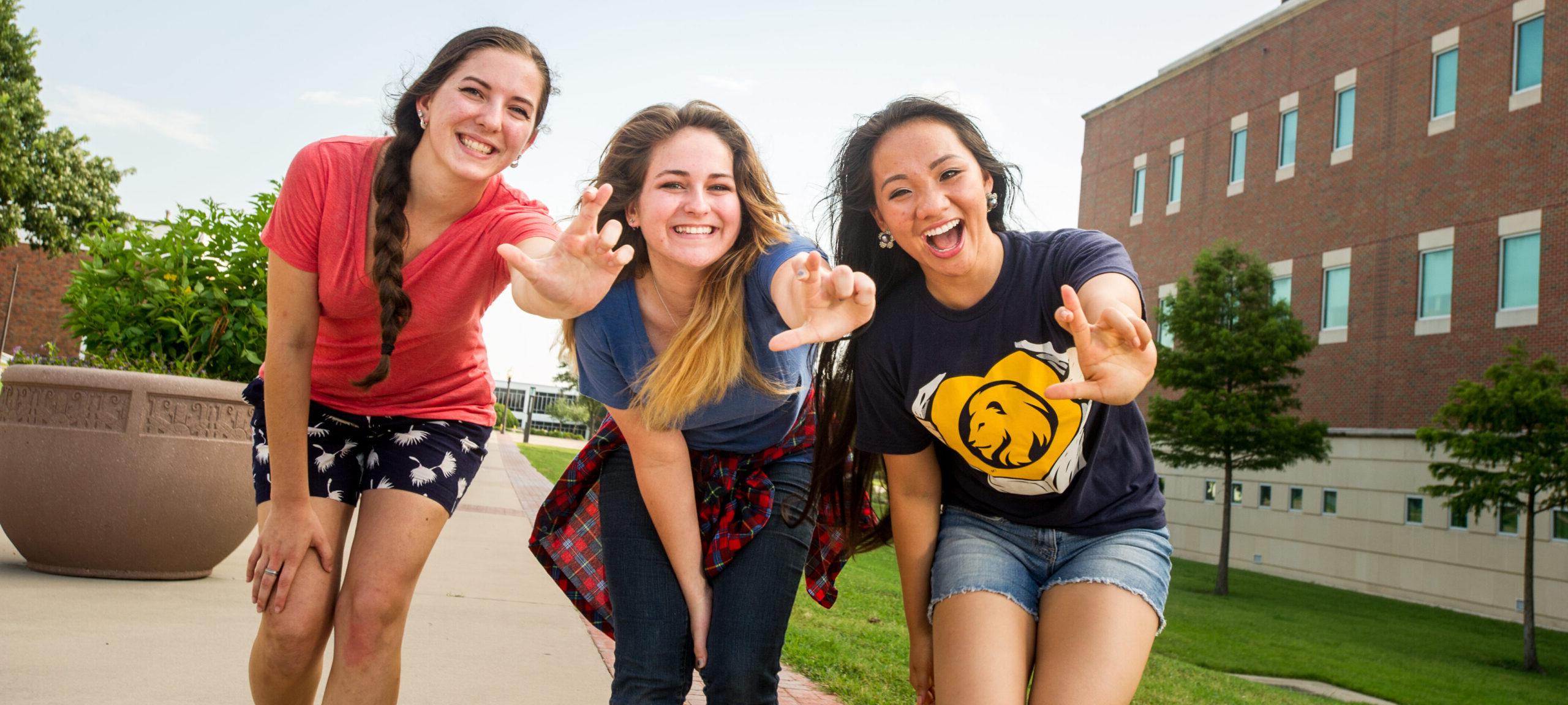 Three female students smiling while showing the leo hand sign.